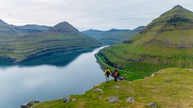 Ziyaretçiler, Faroe Adaları 'ndaki yüksek dağlar ve yemyeşil alanlarla çevrili Gonguturur Hvithamar Patikası boyunca yürürler..