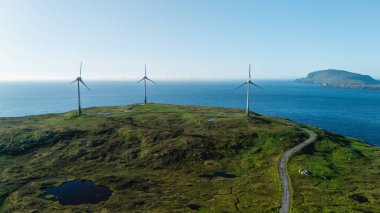 Görkemli rüzgar türbinleri, Faroe Adaları 'nın çarpıcı sahil şeridine bakan yemyeşil tepelerin tepesinde yükseliyor..
