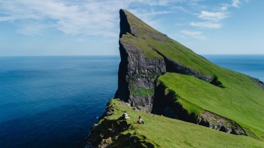 Maceracılar dramatik uçurumlarda otururken Faroe Adaları 'nın çarpıcı güzelliğinin tadını çıkarıyorlar. Bereketli yeşil manzara ve geniş okyanus berrak mavi gökyüzünün altında hayranlık uyandıran bir zemin oluşturur..