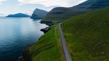 Uçurumları saran dolambaçlı bir yolun olduğu Faroe Adaları 'nın çarpıcı kıyı manzarasını keşfedin. Bereketli yeşil tepeler huzur dolu denize dökülüyor, doğanın güzelliğini ve sükunetini gösteriyor..