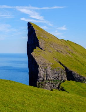 Dramatik Mylingur uçurumları, Kuzey Atlantik 'in sakin mavi sularına bakan canlı yeşil manzaralardan keskin bir şekilde yükselir. Faroe Adaları 'nın güzelliği eşsiz arazisiyle büyülenir..