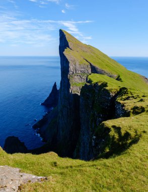 Faroe Adaları 'nın yükselen Mylingur kayalıkları okyanus üzerinde dramatik bir şekilde duruyor, dalgalı yeşil tepeler su kenarına dökülüyor..