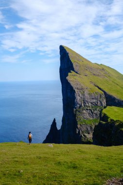 Yalnız bir yürüyüşçü, yemyeşil çimenler ve canlı mavi okyanusla çevrili Faroe Adaları 'nın büyüleyici Mylingur kayalıklarına bakar. Dramatik manzara doğal güzellikleri ve huzuru gözler önüne seriyor..