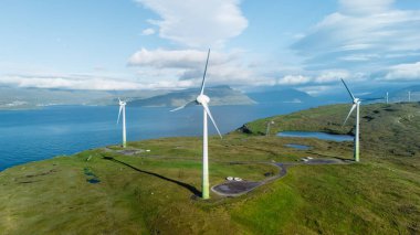 Rüzgar türbinleri, Faroe Adaları 'nın sakin sularına bakan yeşil yamaçların üzerinde görkemli bir şekilde yükselir. Nefes kesici manzara, doğanın yenilenebilir enerji çözümleriyle uyumlu olduğunu gösteriyor..