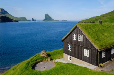 Bour Village, Faroe Adaları 'nın canlı mavi sularına bakan çimen çatılı büyüleyici bir ev. Görkemli uçurumlar berrak bir gökyüzünün altında dramatik bir şekilde yükselir..