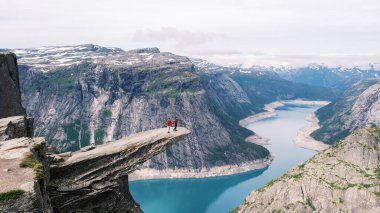 İki maceraperest birey, sakin mavi sulara ve yükselen Norveç fiyortlarına tepeden bakan nefes kesici bir uçurumun üzerinde duruyor. Trolltunga, Norveç