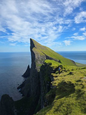 Yürüyüşçüler, Faroe Adaları 'ndaki Mylingur' un engebeli tepelerinden çarpıcı kıyı manzaralarının keyfini çıkarıyorlar. Etrafı dramatik uçurumlar ve açık mavi gökyüzünün altındaki masmavi sularla çevrili..