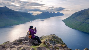Bir gezgin, Faroe Adaları 'ndaki Klakkur' un nefes kesici fiyortlarının ve dağlarının fotoğraflarını çekiyor..