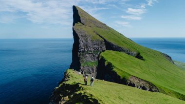 Faroe Adaları 'ndaki yüksek Mylingur kayalıklarının kenarında duran iki yürüyüşçü, Atlantik Okyanusu' na bakıyor..