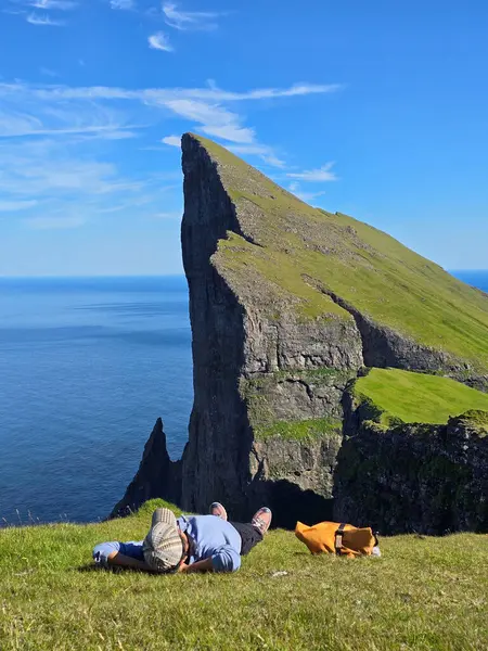 Faroe Adaları 'ndaki Mylingur yürüyüşünden nefes kesici manzaralar, yemyeşil çimlerde dinlenen bir yürüyüşçüyü sergiliyor, dramatik uçurumlar ve açık mavi bir gökyüzünün altında okyanus..
