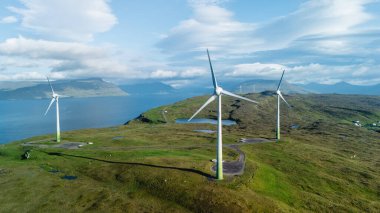 Faroe Adaları 'nın engebeli kıyı şeridi boyunca yer alan rüzgar türbinlerinin büyüleyici görüntüsü.
