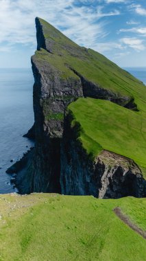 Yükselen Mylingur kayalıkları turkuaz denizin üzerinde dramatik bir şekilde yükseliyor, Faroe Adaları 'nın çarpıcı güzelliğini gözler önüne seriyor..