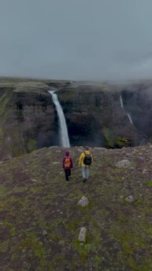 İki maceraperest yürüyüşçü İzlanda 'daki dramatik uçurumların kenarında durup aşağıdaki kanyona düşen Haifoss şelalesini izliyorlar. Sis, manzaraya mistik bir dokunuş ekler..