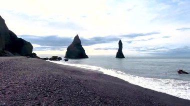 Reynisfjara Sahili İzlanda 'sının benzersiz güzelliğini deneyimleyin. Siyah kumların dramatik bir gökyüzüne karşı yükselen bazalt sütunlarla buluştuğu yer. Dalgalar kıyı boyunca yavaşça çarpar ve sakin bir atmosfer yaratır..