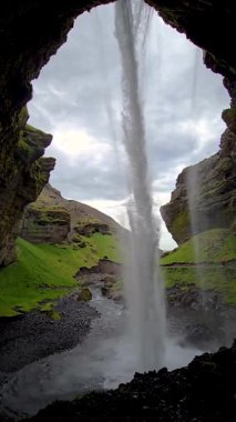 Kvernufoss şelalesinin şelalesinin şelalenin altında zarif bir şelaleyle dalgalanırken yemyeşil tepeler ve büyüleyici İzlanda arka planıyla çevrili olduğunu hissedin..