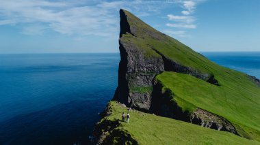 Faroe Adaları 'ndaki Mylingur uçurumunun kıyısında iki maceraperest, büyüleyici okyanus manzarası ve yemyeşil manzaralarla çevrili. Keşif ve keşif için mükemmel bir gün..