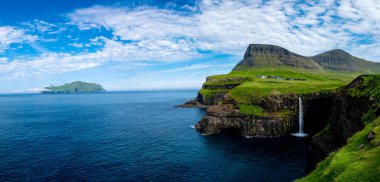 Mulafossur Şelalesi 'nin nefes kesici manzarası Gasadalur köyünün canlı manzarasına karşı okyanusa dökülüyor..