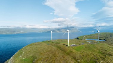 Nefes kesen Faroe Adaları 'nda, yüksek rüzgar türbinleri sakin mavi sulara bakarken doğal enerjiyi kullanırlar..