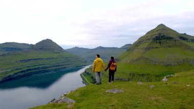İki yürüyüşçü Faroe Adaları 'ndaki Gonguturur Hvithamar Patikası' nın nefes kesici manzarasına hayran kaldılar. Bereketli yeşil dağlar ve sakin sular doğa severler için mükemmel bir atmosfer yaratır..