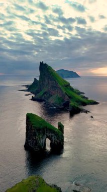 Faroe Adaları 'ndaki Drangarnir uçurumunun dramatik güzelliğini deneyimleyin. Sarp kaya oluşumlarının dingin okyanustan keskin bir şekilde yükseldiği, alacakaranlıkta ham güç ve zarafet sergileyen doğa..