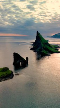 Drangarnir 'in görkemli kayalıkları Kuzey Atlantik' in sakin sularından dramatik bir şekilde yükseliyor. Titreyen gökyüzü sakin yüzeye yansıyarak nefes kesici bir kıyı manzarası yaratıyor..