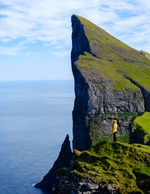 Issız bir figür yemyeşil bir Mylingur uçurumunda duruyor, çarpıcı bir kaya oluşumuna bakıyor ve Faroe Adaları 'nın okyanusuna çarpıyor.
