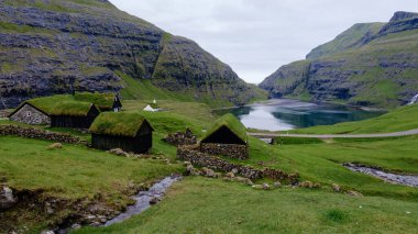 Bereketli bir vadiye yerleşmiş, geleneksel otlaklarla kaplı evler Faroe Adaları 'ndaki sakin bir gölün sakin kıyılarını kaplıyor. Saksun Köyü