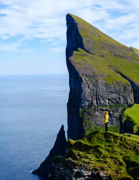Issız bir figür yemyeşil bir Mylingur uçurumunda duruyor, çarpıcı bir kaya oluşumuna bakıyor ve Faroe Adaları 'nın okyanusuna çarpıyor.