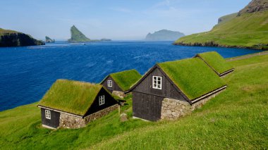Çimen çatılı tuhaf kulübeler yemyeşil tepelere yuva kurarak huzurlu suları ve Faroe Adaları 'nın dramatik uçurumlarını nefes kesen manzaralar sunuyor. Bour Köyü