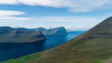Faroe Adaları 'nda nefes kesici uçurumlar ve canlı mavi sular keşfedin. Bu büyüleyici manzara, adaların eşsiz coğrafyasını gözler önüne seriyor ve hayranlarını doğal güzelliklerini keşfetmeye çağırıyor..