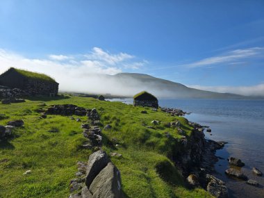 Faroe Adaları 'nın kıyı şeridi boyunca geleneksel taş kulübelerin bulunduğu sakin bir manzara..