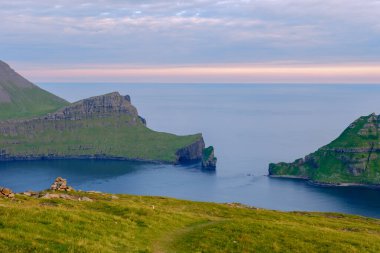 Canlı yeşil uçurumlar durgun denizden dramatik bir şekilde yükselir ve gün batımında Faroe Adaları 'nda nefes kesici bir manzara yaratır. Doğayı, güzelliği ve huzuru yansıtan huzurlu bir manzara..