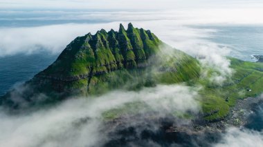 Bu nefes kesen manzara, göksel bulutlar ve derin mavi Atlantik Okyanusu ile çevrili yeşil dağ tepelerini gözler önüne seriyor. Drangarnir uçurumları Faroe Adaları