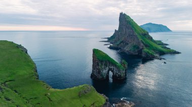 Drangarnir uçurumları Faroe Adaları 'ndaki Atlantik Okyanusu' ndan alacakaranlıkta yumuşak, pastel bir gökyüzünün altında dramatik bir şekilde yükselir. Bu sakin manzara doğayı, güzelliği ve engebeli cazibeyi yakalar..