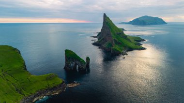 Dramatik Drangarnir uçurumları sakin denizden yükseliyor, gün batımında verimli yeşilliklerle kaplı Faroe adaları tarafından.