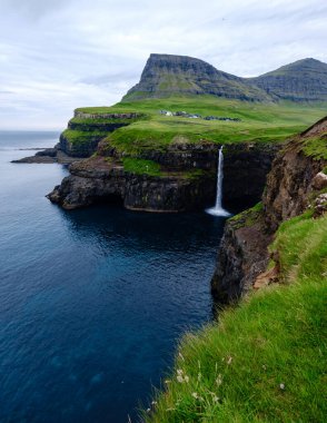 Şelale dik uçurumlardan aşağı yuvarlanarak Atlantik Okyanusu 'nun sakin mavi sularına akar. Bereketli yeşil çimenler, Gasadalur köyü Faroe Adaları yakınlarındaki Mulafossur şelalesi manzarayı kaplar.