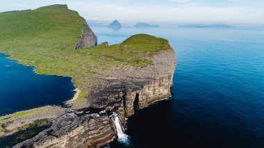 Faroe Adaları 'ndaki sakin suların üzerinde şelalelerle bezenmiş nefes kesen uçurumlar dramatik bir şekilde yükselir. Sahne, bu uzak cennette bulunan sükuneti ve doğal güzelliği yakalıyor..
