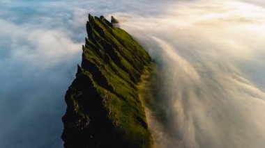 Faroe Adaları 'ndaki yüksek uçurumlar bulutları delip gerçeküstü bir atmosfer yaratıyor. Bereketli yeşil çimenler, gün doğumunda sersemleten doğayla çelişiyor..