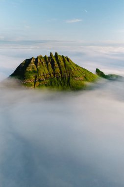 Faroe Adaları 'nın göbeğine yerleşmiş bu çarpıcı dağ zirveleri, şafak vakti soluk kesen güzellik ve sükuneti gösteren yumuşak bulutlardan oluşan bir battaniyeden çarpıcı bir şekilde ortaya çıkar..