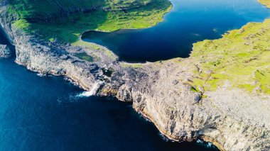 Faroe Adaları 'nın dramatik uçurumlarını ve dingin sularını gösteren canlı hava perspektifi, gün batımında doğal güzellik ve canlı yeşilliklerin çarpıcı etkileşimini vurguluyor. Sorvagsvatn Gölü