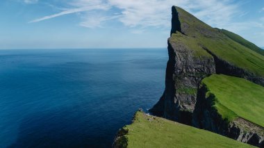 Büyüleyici Mylingur kaya oluşumları Faroe Adaları 'ndaki derin mavi okyanusa karşı çarpıcı bir şekilde yükselir. Yemyeşil tepeler uçurumun kenarını sarar, gökyüzü ile büyüleyici bir kontrast yaratır..