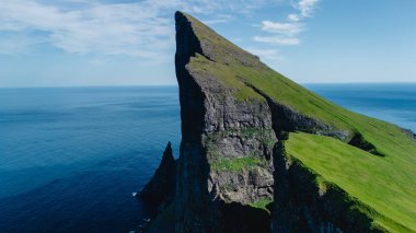 Faroe Adaları 'ndaki Atlantik Okyanusu' nun canlı mavi sularından dramatik bir uçurum keskin bir şekilde yükselir. Bereketli yeşillik kayalık kenarlarla çelişiyor ve nefes kesici bir doğal manzara yaratıyor..