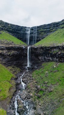 Faroe Adaları 'ndaki engebeli uçurumların üzerinden akan Fossa şelalelerinin nefes kesici manzarası. Bereketli yeşil manzara doğal güzelliği artırıyor, sakin bir atmosfer yaratıyor..