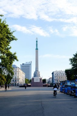 Riga, Letonya, 26 Ağustos 2025. İkonik Özgürlük Anıtı şehrin kalbinde dimdik duruyor. Yerliler ve ziyaretçiler geniş cadde boyunca bisiklet sürüyorlar.