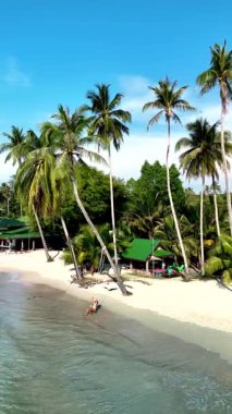 Tayland 'ın Koh Kood Adası' nda sallanan palmiyeler ve sakin sularla dolu sakin bir sahil. Ziyaretçiler sıcak güneşin ve huzurlu atmosferin tadını çıkarırlar, cennette dinlenmek için mükemmeldirler..
