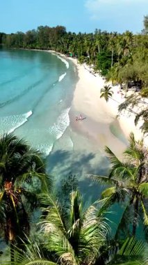 Koh Kood Adası 'ndaki yumuşak beyaz kum ve turkuaz suların çarpıcı manzarası. Palmiye ağaçları nazikçe sallanıyor, ziyaretçiler sakin sahil atmosferinin tadını çıkarıyorlar. Plajda tatilde olan bir çift kadın ve erkek.