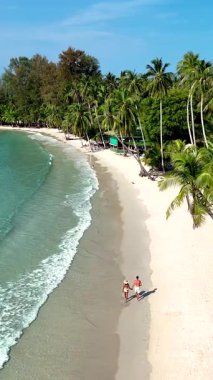 Tayland 'daki Koh Kood Adası' nın nefes kesici güzelliğini keşfedin. Yumuşak kumlu kıyıları kucaklayan nazik dalgalar. Birkaç Asyalı kadın ve Kafkasyalı erkek tatilde.