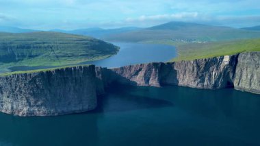 Sakin sulara dalan, Faroe Adaları 'nın engebeli güzelliğini gösteren nefes kesici uçurumları keşfedin. Açık mavi gökyüzü altında, doğanın mükemmel bir karışımı güç ve sakinlik..