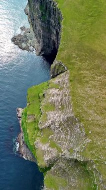 Dramatik uçurumların ve sakin denize bakan canlı yeşil yamaçların olduğu Faroe Adaları 'nın çarpıcı manzarasını keşfedin. Gün ışığında doğanın görkeminin mükemmel bir örneği..