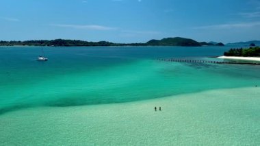 Turkuaz sular Tayland 'daki Koh Kham Adası' nın beyaz kumlu plajına çarpar. Sakin manzaralar rahatlamak için mükemmel bir tropikal cennet yaratıyor. Birkaç beyaz erkek ve Asyalı kadın tatilde.